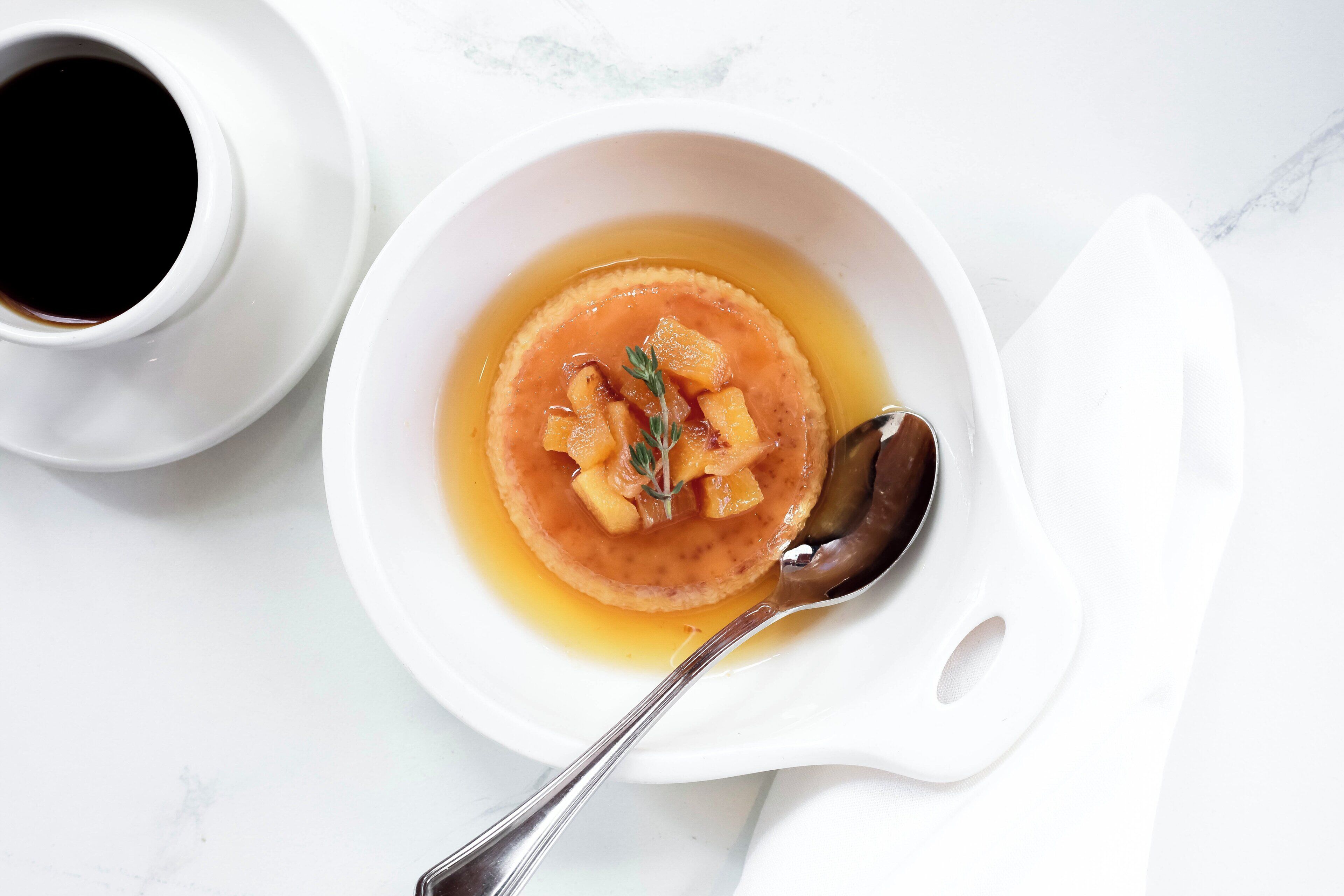 A bowl of soup with a spoon, a cup of coffee, and a napkin on a white surface.