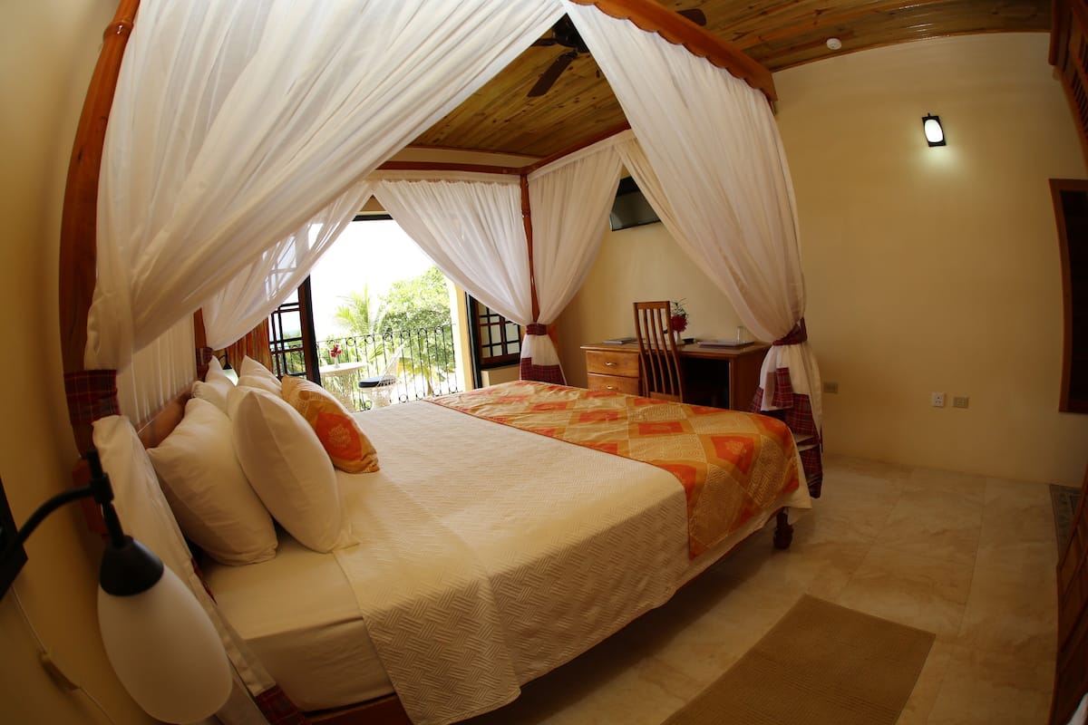 A bedroom with a four-poster bed, a desk, and a chair.