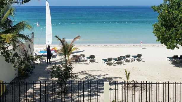 A beach with white umbrellas, lounge chairs, and a clear blue sky.