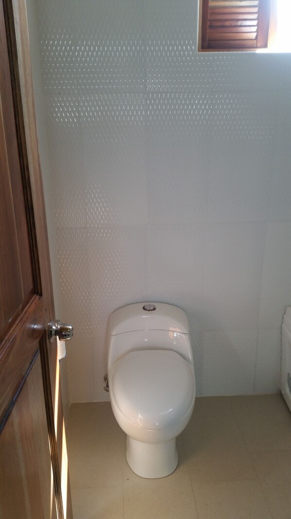 A white toilet in a bathroom with a wooden door and a window with blinds.