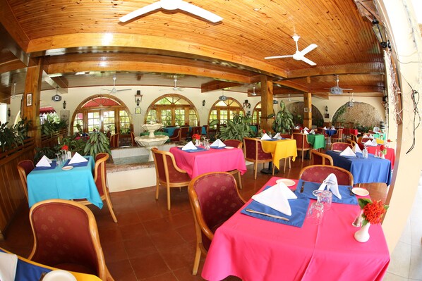 A restaurant with multiple tables, wooden ceiling, and arched windows. - Charela Inn Hotel (Negril)