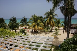 A beach view with palm trees, a wooden pergola, and a sandy area with lounge chairs. - Charela Inn Hotel (Negril)