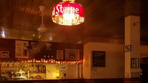 A cozy bar area with wicker furniture, a bar counter with bottles, and a neon sign.