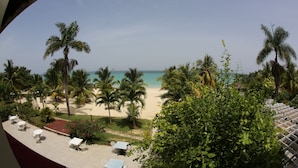 Une vue sur la plage, avec des palmiers, un espace piscine et un patio couvert équipé de tables et de chaises.
