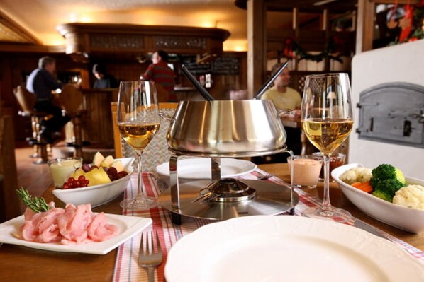 Una mesa de comedor con una olla para fondue, copas de vino y platos de comida.