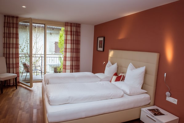 A double bed with white linens, a bedside table with a book, and a view of a balcony with a chair. - Hotel Restaurant Weinstube (Eschen)