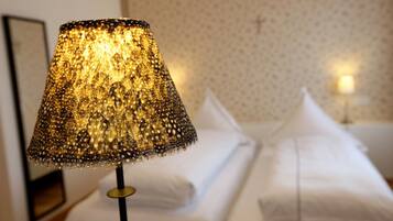 A lamp with a textured lampshade, a neatly made bed with pillows, and a wall with a subtle pattern.