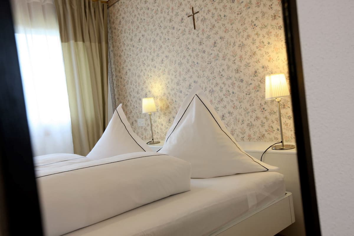 Una cama bien hecha con sábanas blancas y dos almohadas, un fondo de papel tapiz floral y dos lámparas de noche.