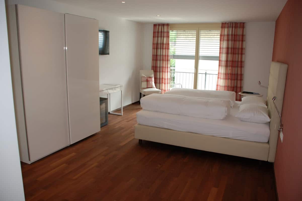 Un dormitorio con cama, armario, escritorio, silla y ventana con cortinas.