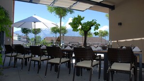 An outdoor dining area with wicker chairs and tables, a large umbrella, and a view of mountains. - Hotel Restaurant Weinstube (Eschen)