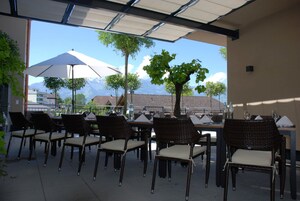 Un espacio de comedor al aire libre con sillas y mesas de mimbre, un paraguas grande y vistas a las montañas.