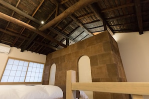 A room with a high wooden ceiling, a large window with a grid pattern, and a bed with a wooden headboard.