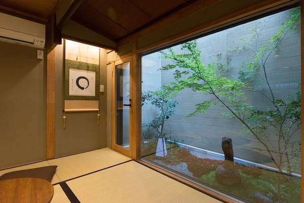 A traditional Japanese room with tatami flooring, a shoji screen door, and a view of a garden with a tree and rocks.