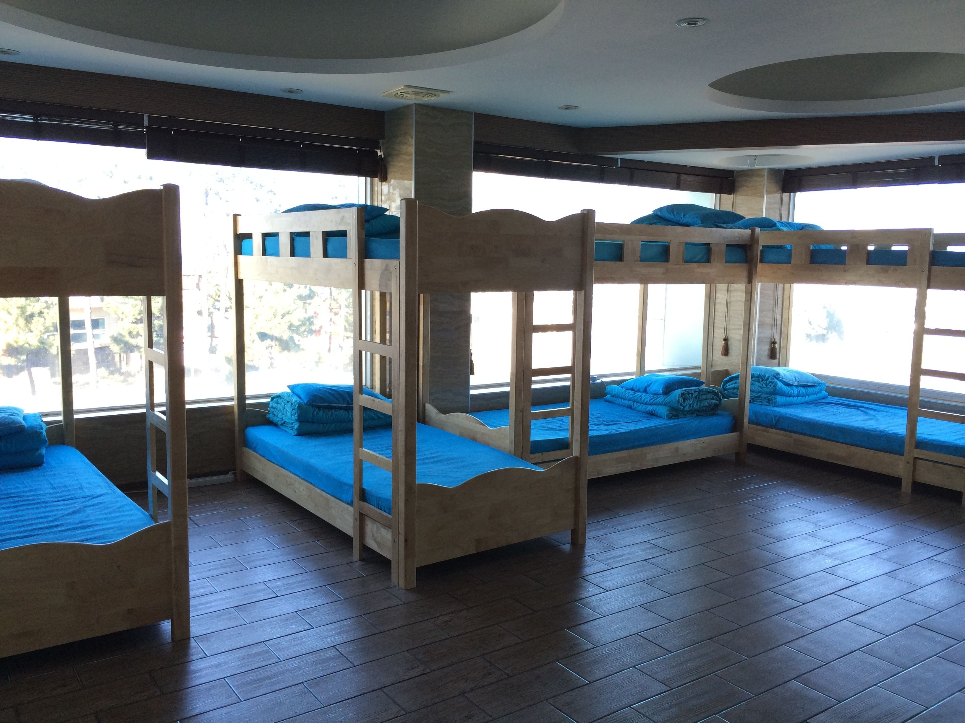 Quarto com beliches, piso de madeira e grandes janelas.