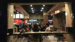 Een restaurantinterieur met houten wanden, een balie en verschillende gasten die aan tafels zitten.