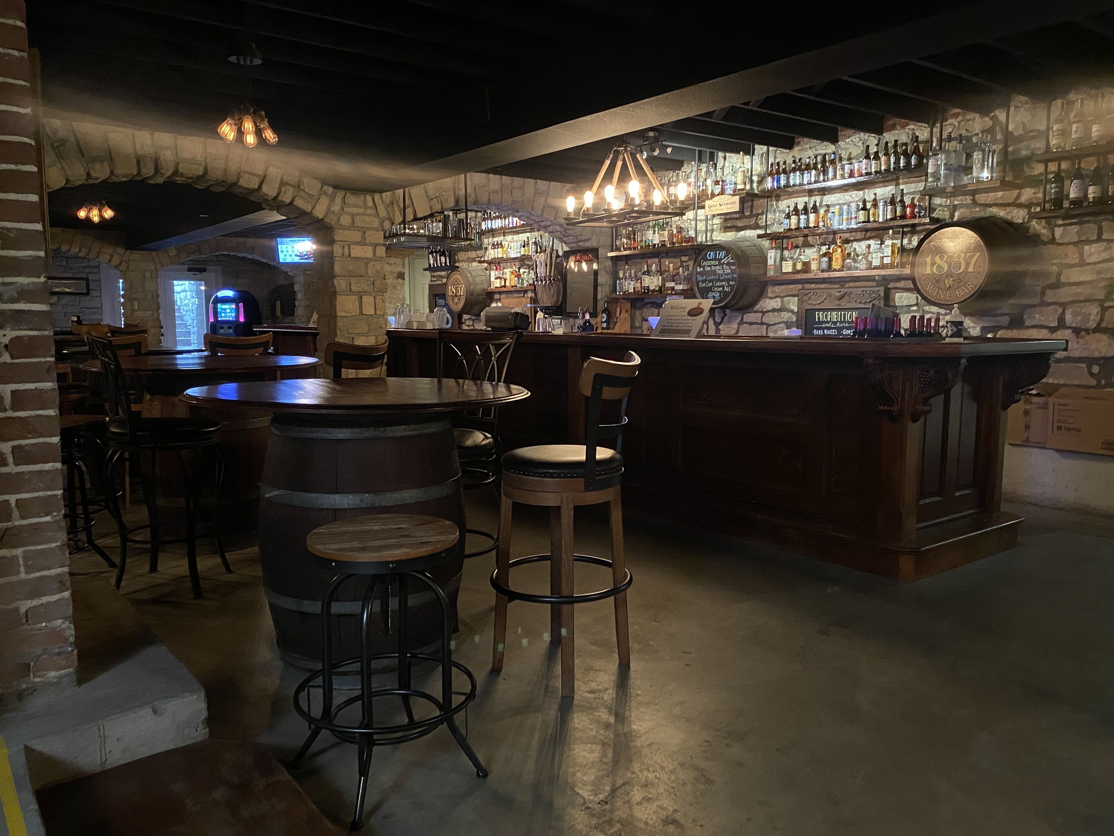 Un espace bar avec des tabourets de bar en bois, un mur en pierre et une variété de bouteilles exposées sur des étagères.