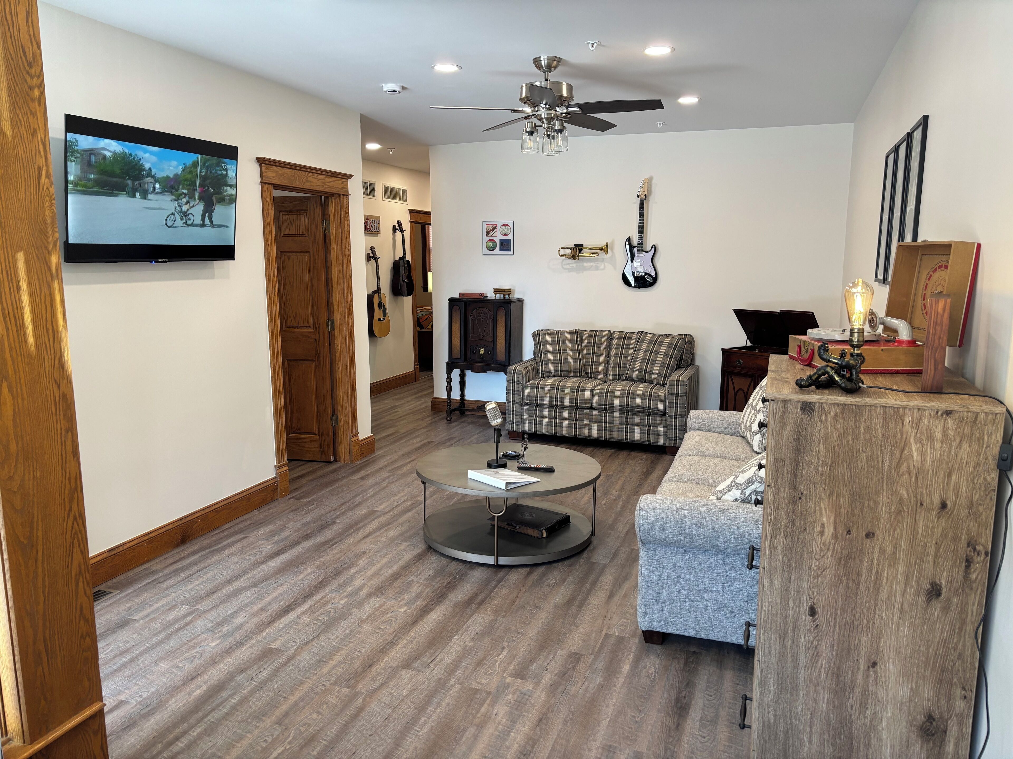 A living room with a plaid sofa, a round coffee table, a wooden sideboard, and a ceiling fan.