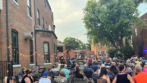 An outdoor seating area with brick buildings, tables, and chairs. - Hermann Crown Suites (Hermann)