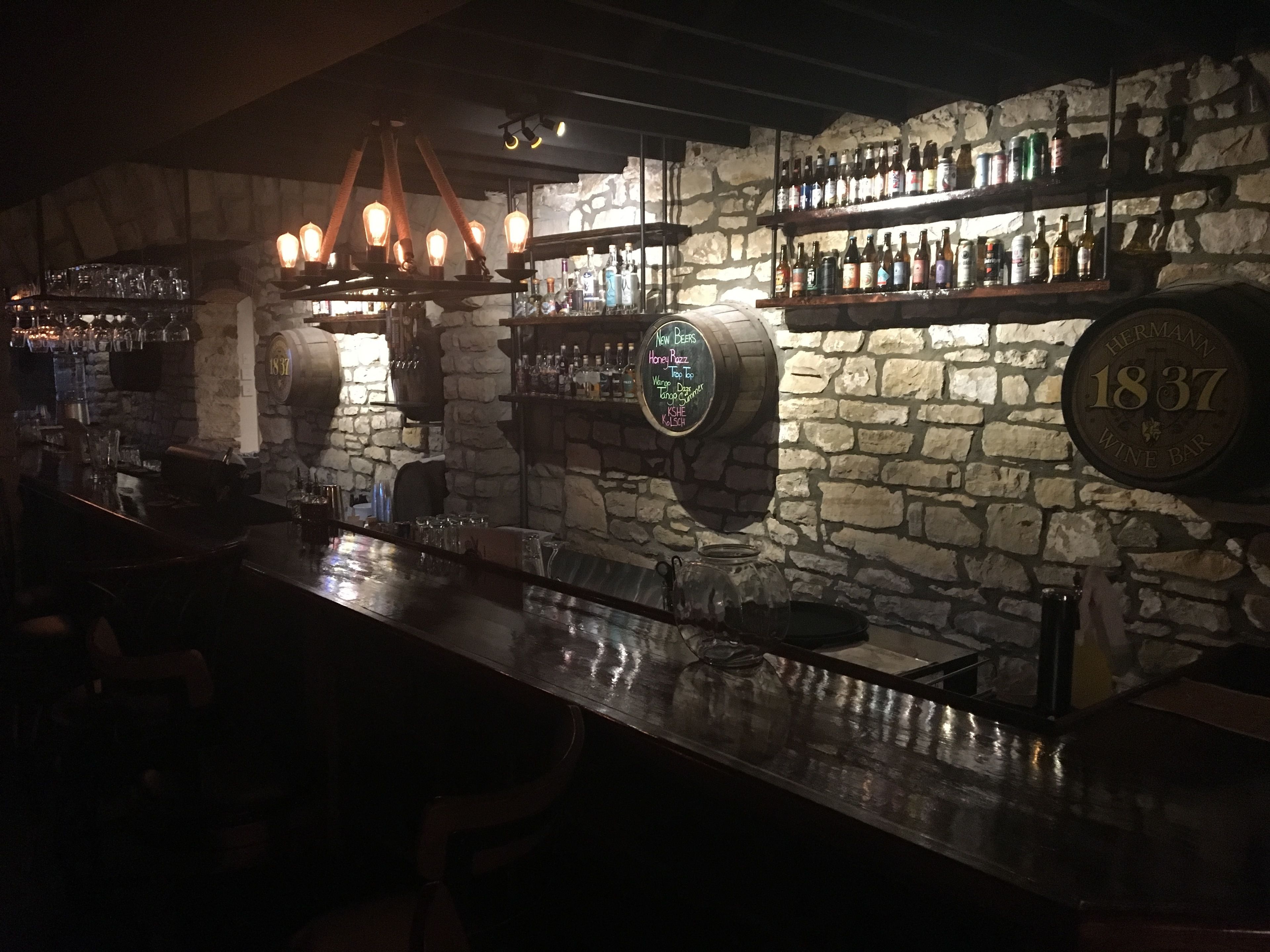 Un bar con paredes de piedra, estanterías llenas de botellas y una grifería de cerveza antigua.