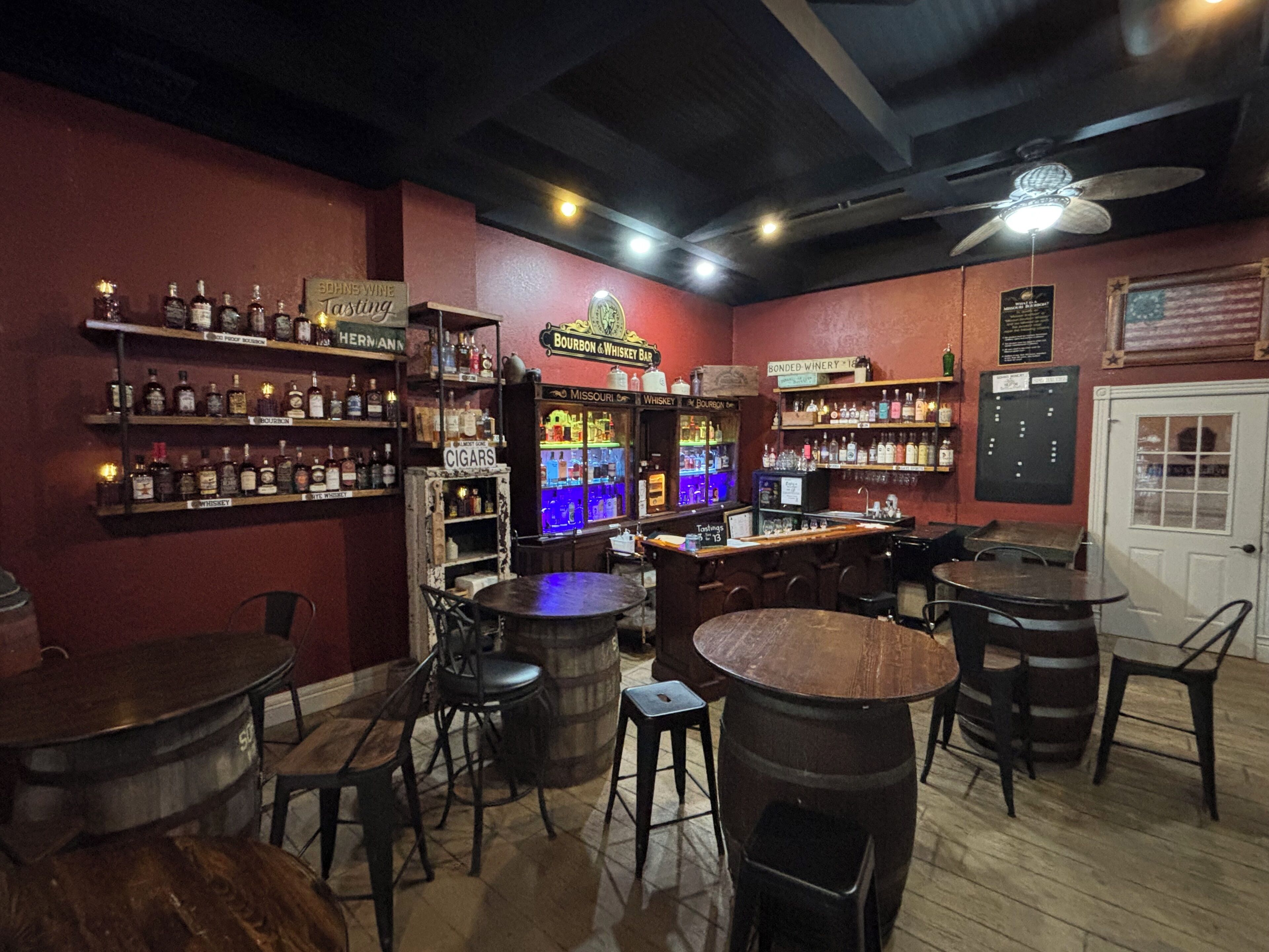 Un bar avec des meubles en bois, des étagères remplies de bouteilles d’alcool et une enseigne indiquant « bourbon » et « whisky ».