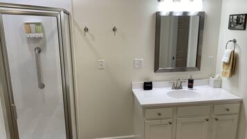 A bathroom with a shower, a sink, a mirror, and a towel rack.