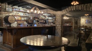 A bar with a stone wall, wooden bar counter, and round tables. - Hermann Crown Suites (Hermann)