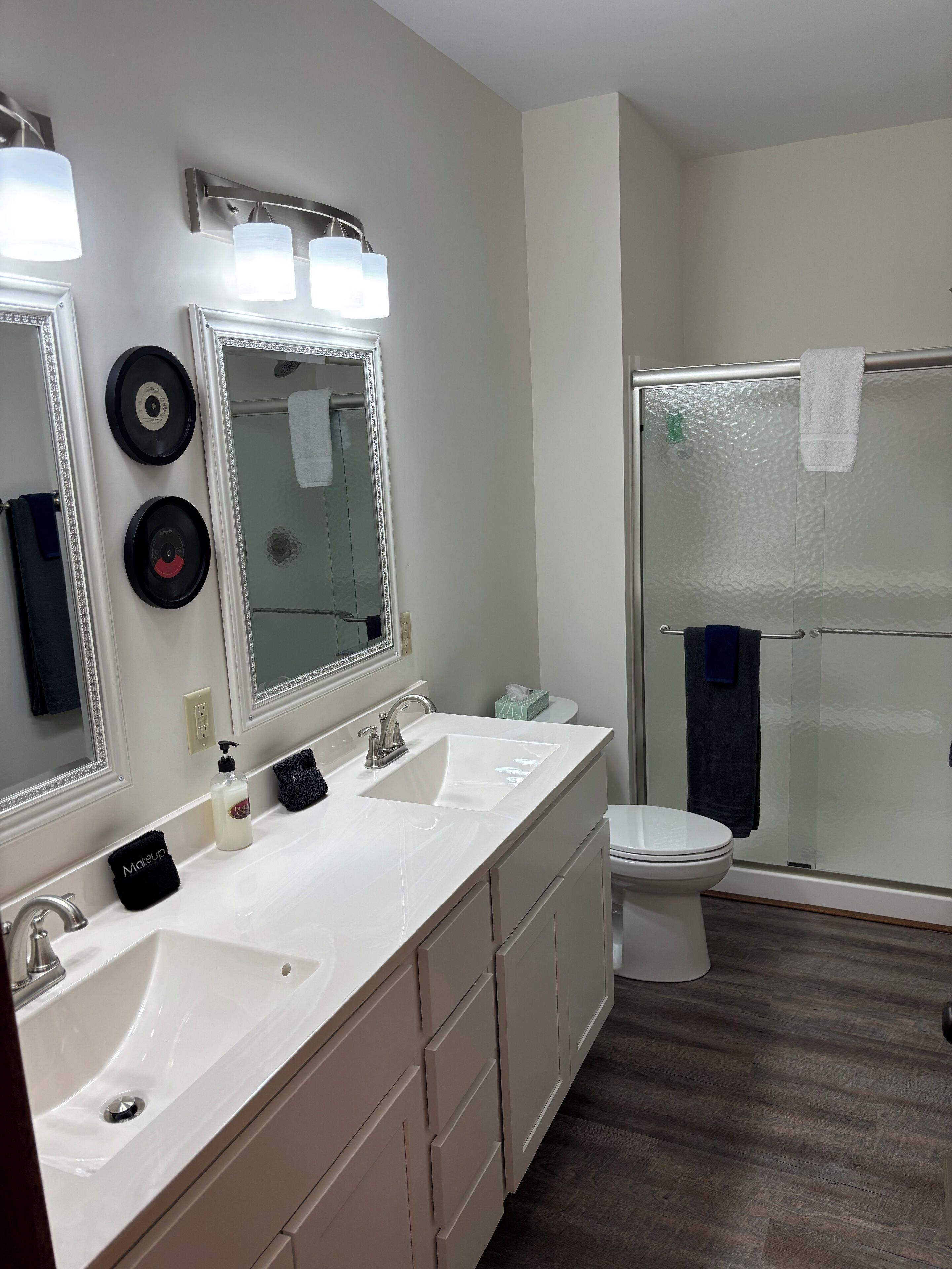 A modern bathroom with dual sinks, a large mirror, and a glass-enclosed shower.