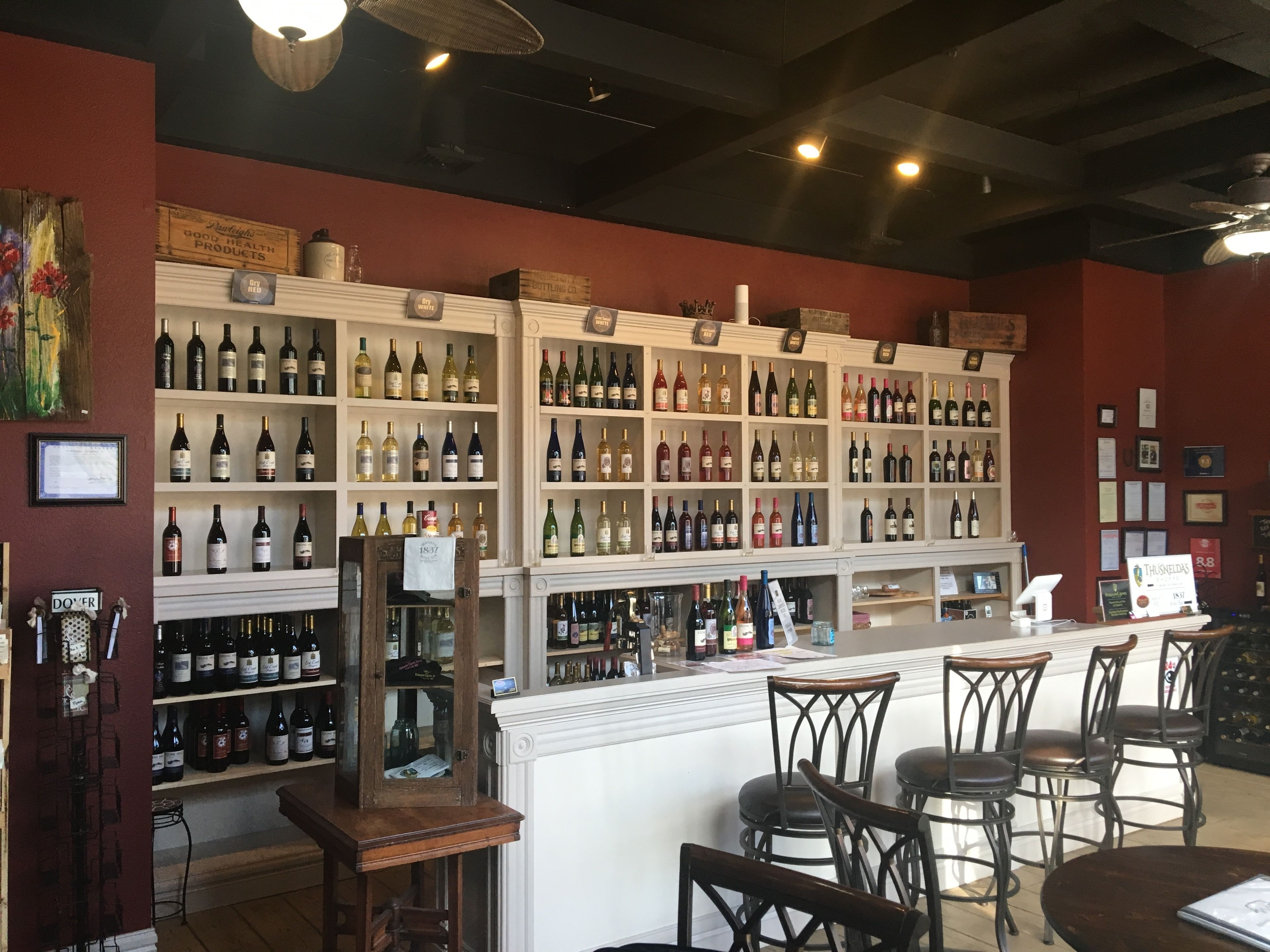 A bar area with shelves of wine bottles, a wooden counter, and several chairs.