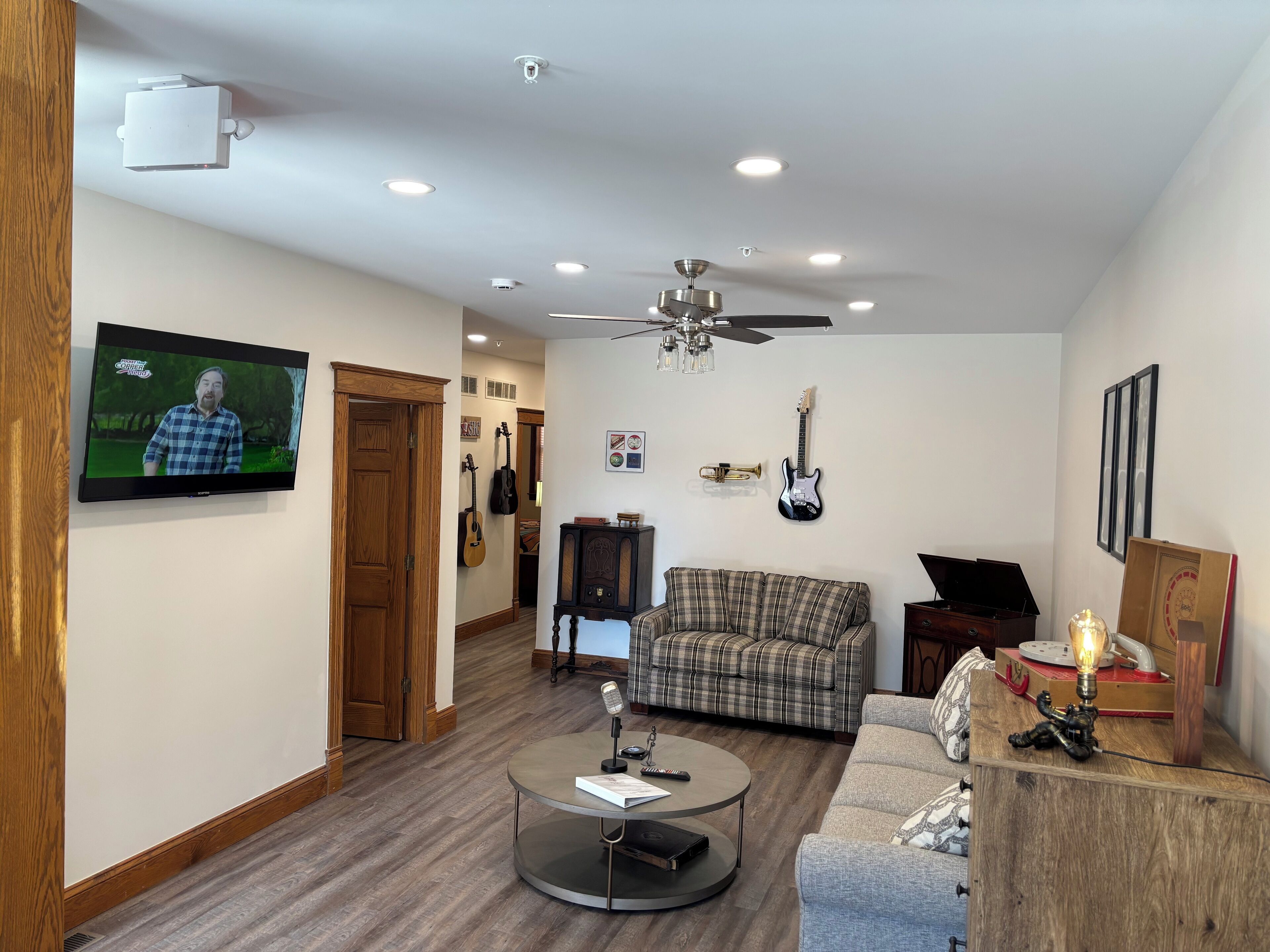 A living room with a television, a ceiling fan, a couch, a coffee table, and musical instruments.