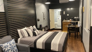 A modern bedroom with a bed, bedside table, and a small seating area with a chair. - Hermann Crown Suites (Hermann)