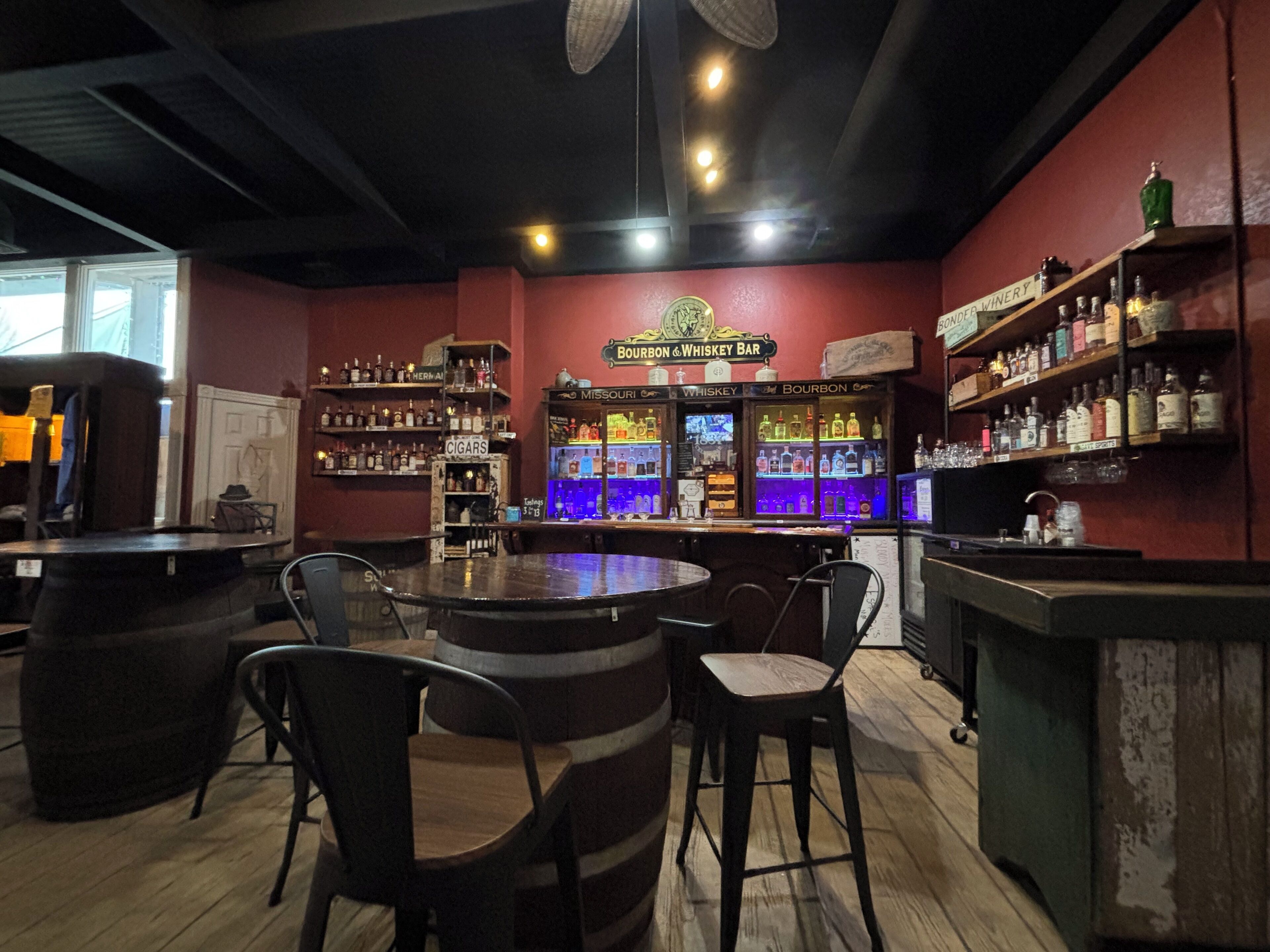 A bar area with wooden barrels, bar stools, and shelves stocked with liquor.