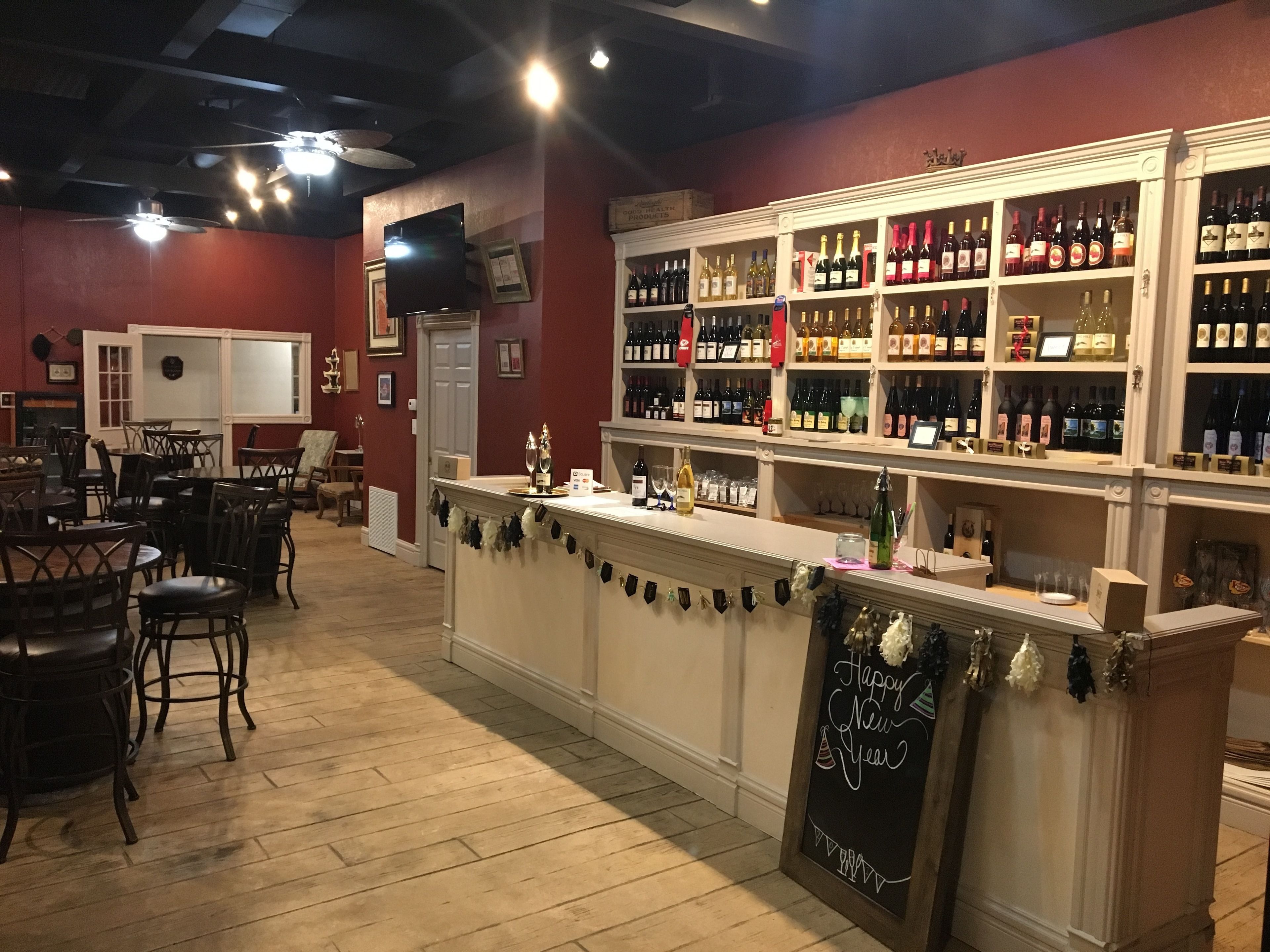 Un espace bar avec des chaises et des tables en bois, un comptoir orné d’une pancarte « Bonne année », et des étagères remplies de bouteilles de vin.