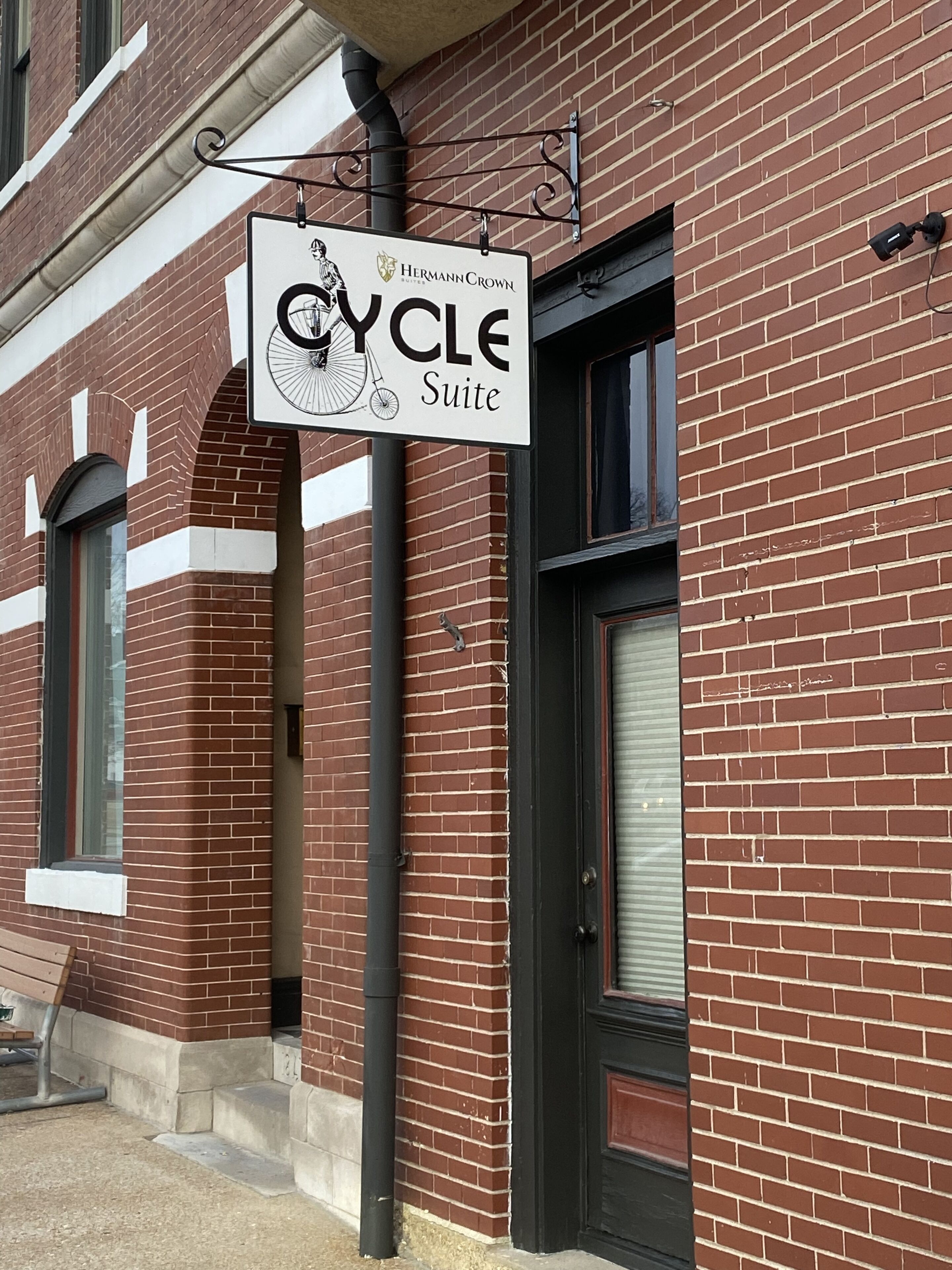 A brick building with a sign for "Hermann Crown Suites" and a bicycle symbol, indicating a cycling facility.