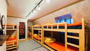 A dormitory room with bunk beds, a mirror, a patterned rug, and a window with curtains.