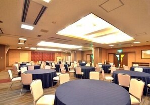 Une salle de conférence dotée de plusieurs tables rondes, chacune entourée de chaises, dans un espace bien éclairé, avec un plafond haut et un aménagement moderne.