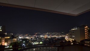 Une vue nocturne d’une ville, prise depuis un point d’observation élevé, avec des bâtiments illuminés et une vue lointaine de la ville.