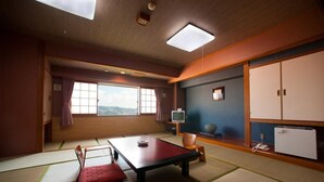 Une pièce de style japonais traditionnel, avec un sol recouvert de tatamis, une petite table basse avec des coussins, un téléviseur et une armoire.