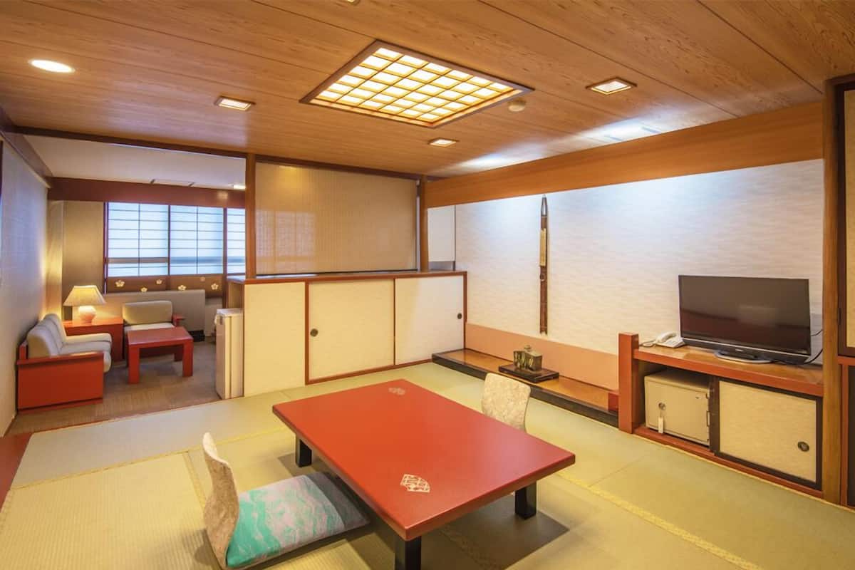 Una habitación tradicional japonesa con suelo de tatami, una mesa baja, un sofá y un televisor sobre un mueble de madera.