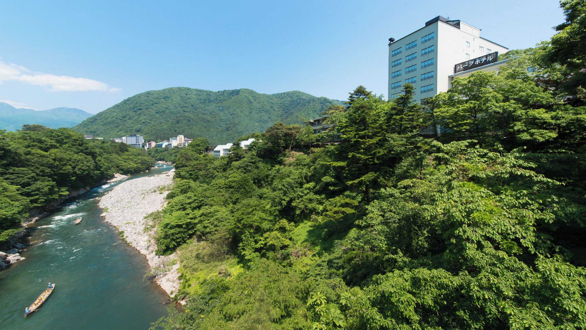 A river with a boat, surrounded by dense green forest and a building with a sign in a foreign language.