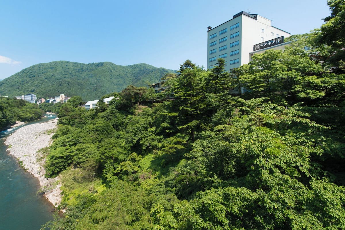 Un río con un bote, rodeado de un denso bosque verde y un edificio con un letrero en un idioma extranjero.