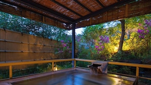 A hot tub with a wooden deck and bamboo walls, surrounded by lush greenery and flowering plants. - Kinugawa Park Hotels (Nikko)