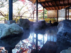 A traditional Japanese onsen with large rocks, a wooden structure, and a view of autumn trees. - Kinugawa Park Hotels (Nikko)