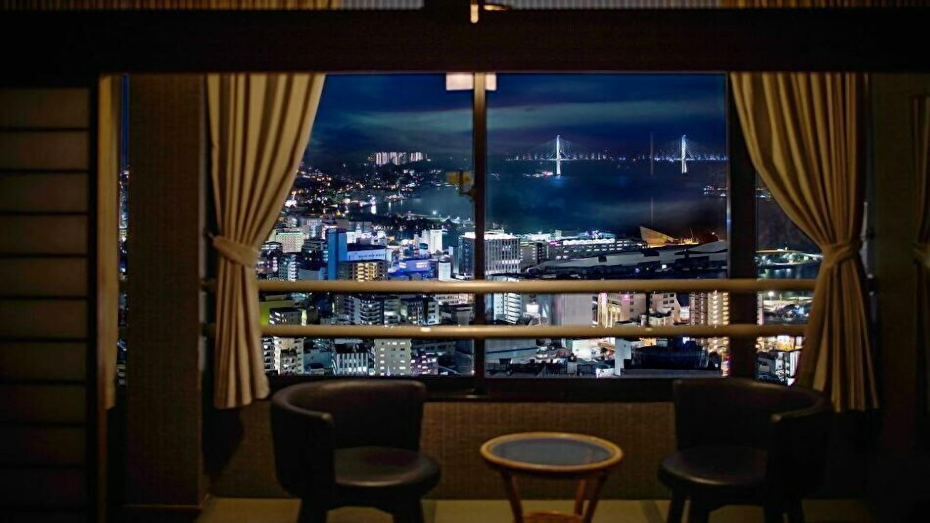 Una habitación con un amplio ventanal que ofrece vistas a un paisaje urbano nocturno, incluyendo un puente y edificios.