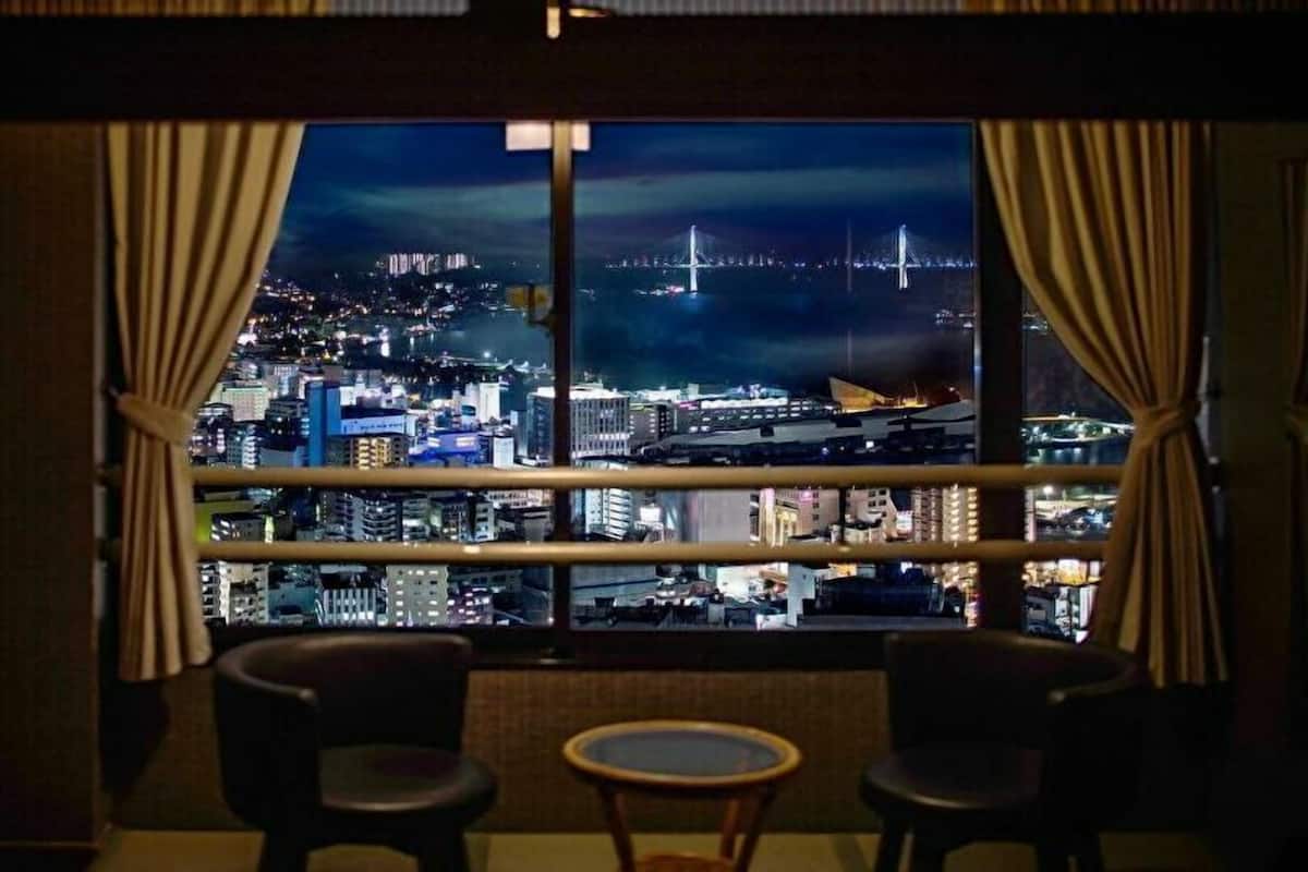 Una habitación con un amplio ventanal que ofrece vistas a un paisaje urbano nocturno, incluyendo un puente y edificios.