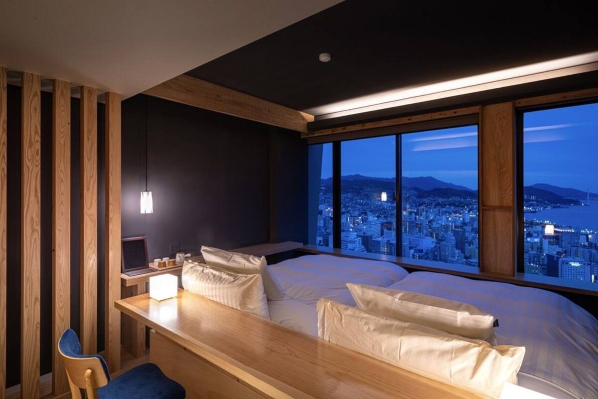 Un dormitorio moderno con vista a la ciudad, un escritorio de madera y una cama con ropa de cama blanca.