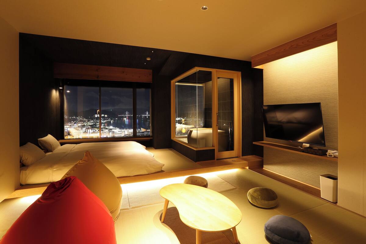 Una habitación de hotel moderna con una cama grande, un sofá, un televisor y vistas a la ciudad desde la ventana.