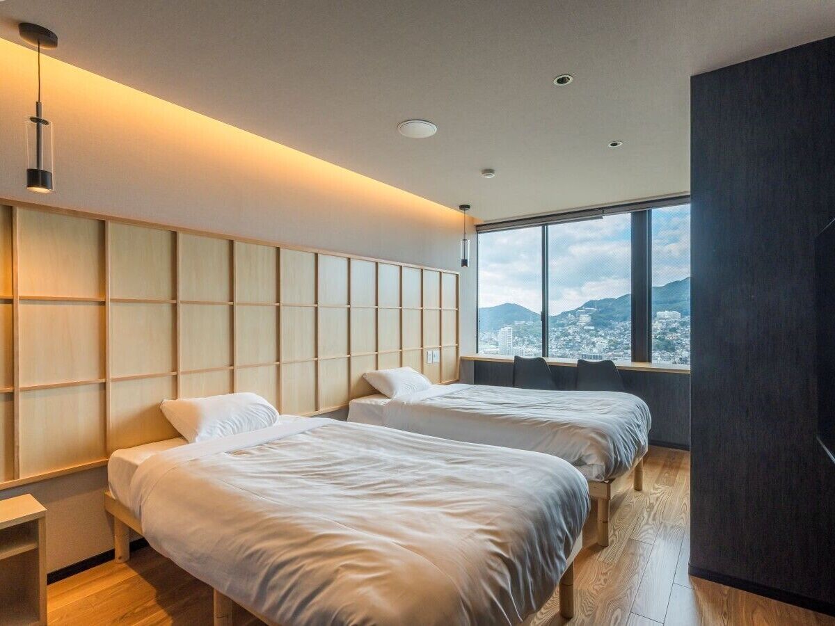 Una habitación de hotel moderna con dos camas, un ventanal con vista a la ciudad y un panel de pared de madera.