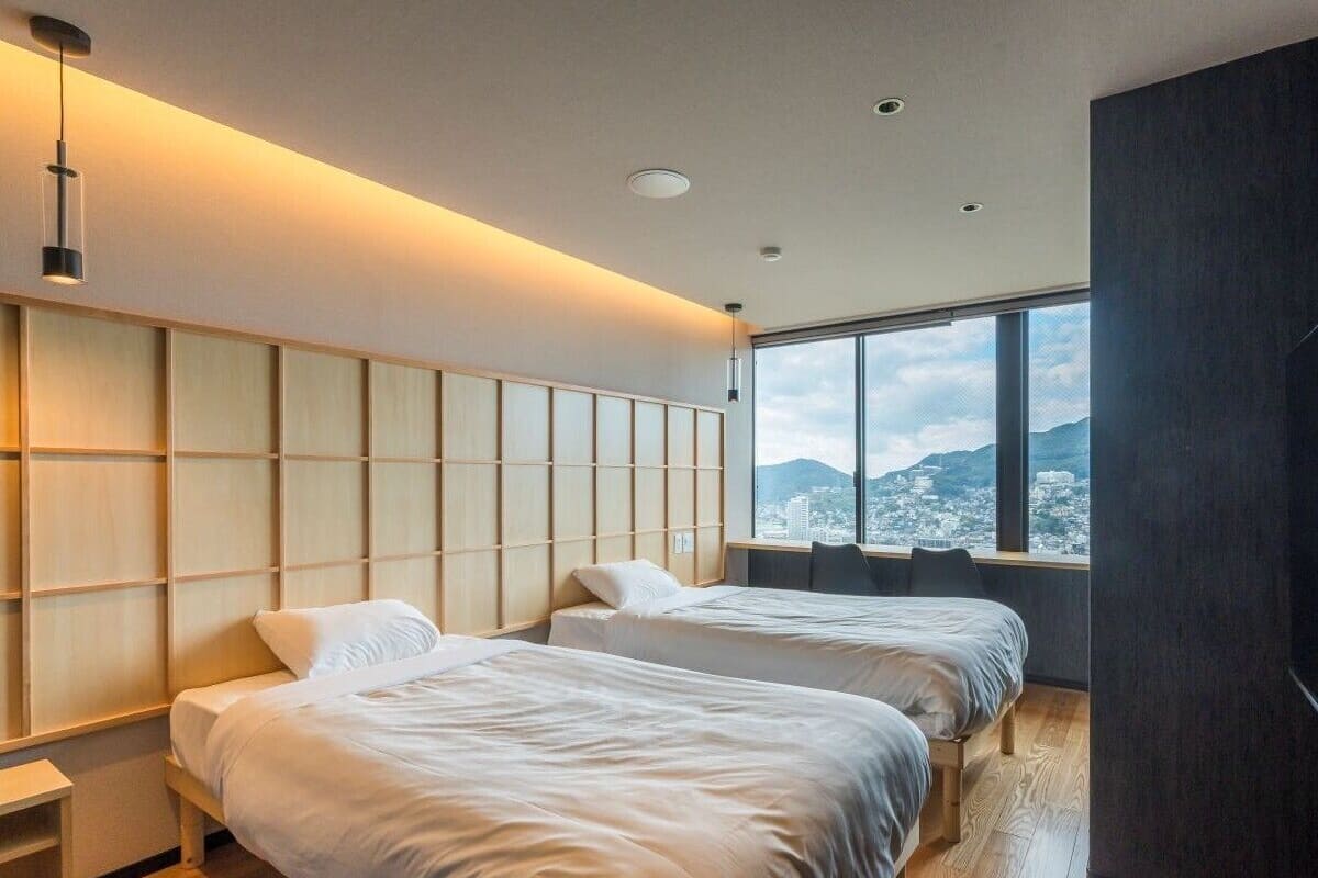 Una habitación de hotel moderna con dos camas, un ventanal con vista a la ciudad y un panel de pared de madera.