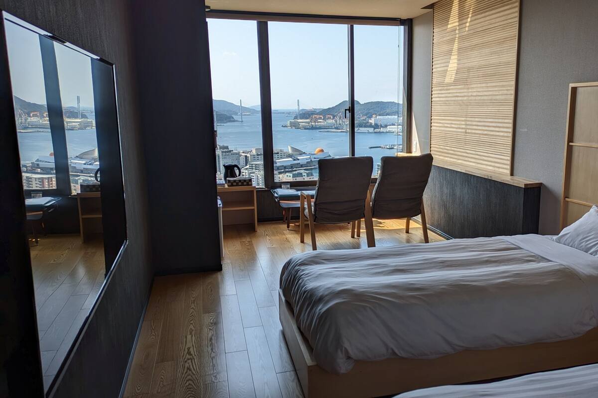 Habitación de hotel con una cama grande, un escritorio, dos sillas y vistas a la ciudad y al agua.