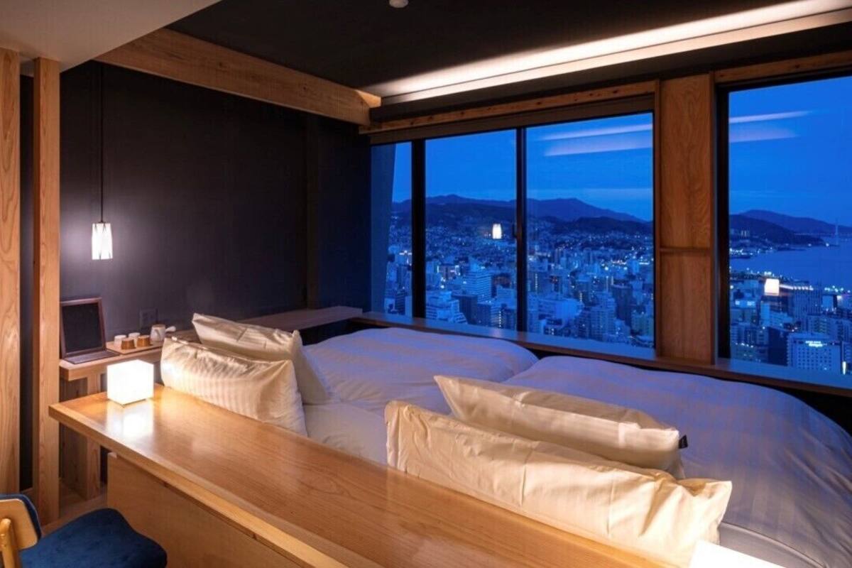 Un dormitorio con una cama grande, un escritorio y vistas a una ciudad al atardecer.